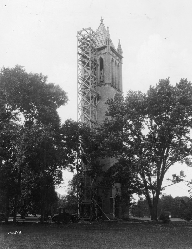 The Campanile with a wooden tower built against one side. An automobile and some construction debris are at the bottom of the tower. The tower is for the purpose of installing a new bell in The Campanile.