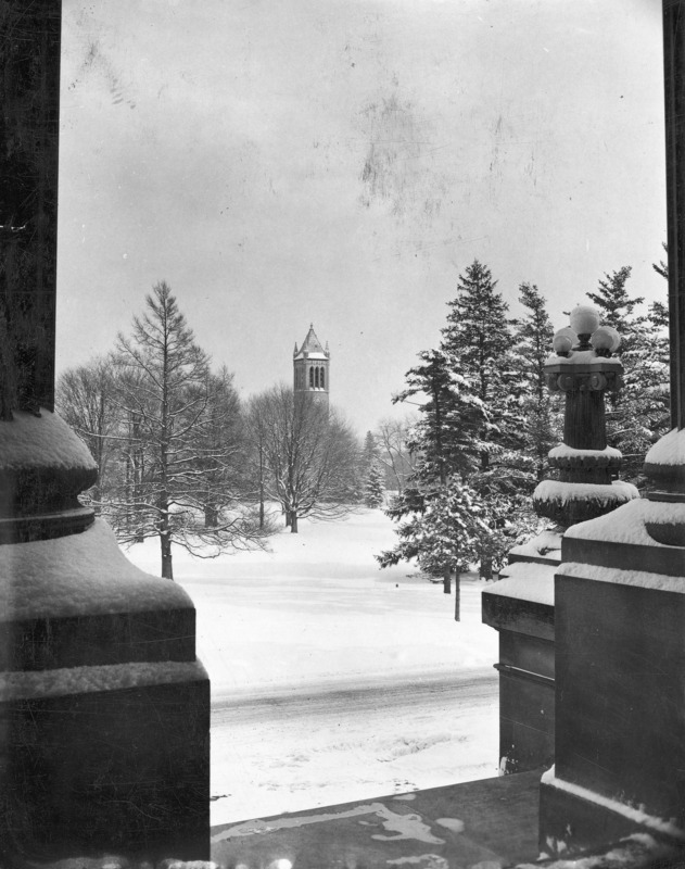 The Campanile in winter as seen from under the portico of Beardshear Hall. Buildings, trees, and ground are snow covered.