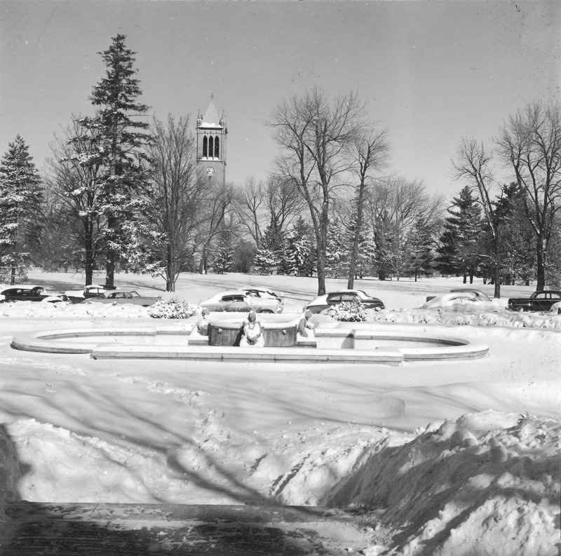 Central campus in winter. A snow covered fountain (Christian Petersen's Fountain of the Four Seasons) as viewed from the north steps of the Memorial Union lies in the middle distance, with the Campanile in the background. Snow covered cars line the street. One of a set of five winter photographs, the others of which are: 4-8-I.Campanile.230-7-6-1; 4-8-I.Campanile.230-7-6-2 [not digitized]; 4-8-I.Campanile.230-7-6-4; and 4-8-I.Campanile.230-7-6-5.