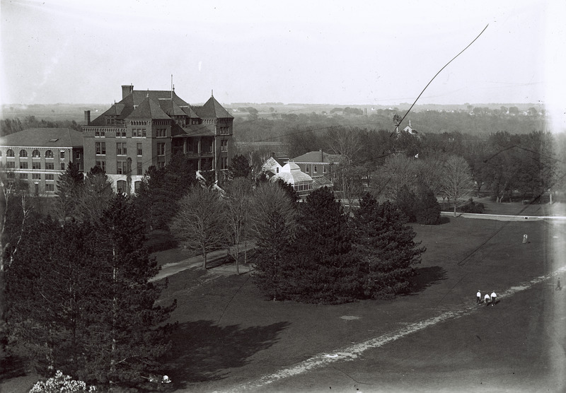 An aerial view of Catt Hall. The Farm Mechanics Lab, Old Horticulture Lab, greenhouse, Engineer's Cottage and a small portion of the old Cattle Barn are visible.