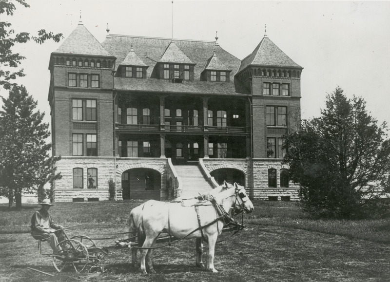 The front of Catt Hall. In the foreground is a driver and a team of Percherons drawing a piece of lawn equipment.