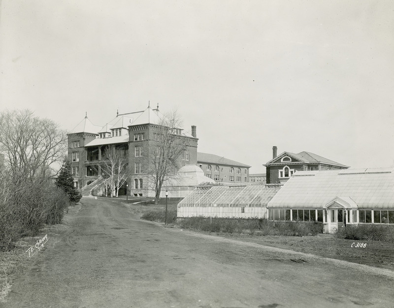 The front and side of Catt Hall. Greenhouses can be seen in the foreground.