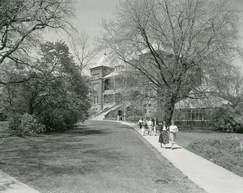 Several students walking along a path leading away from Catt Hall, which can be seen in the background. The greenhouse is directly to the right of Catt Hall.