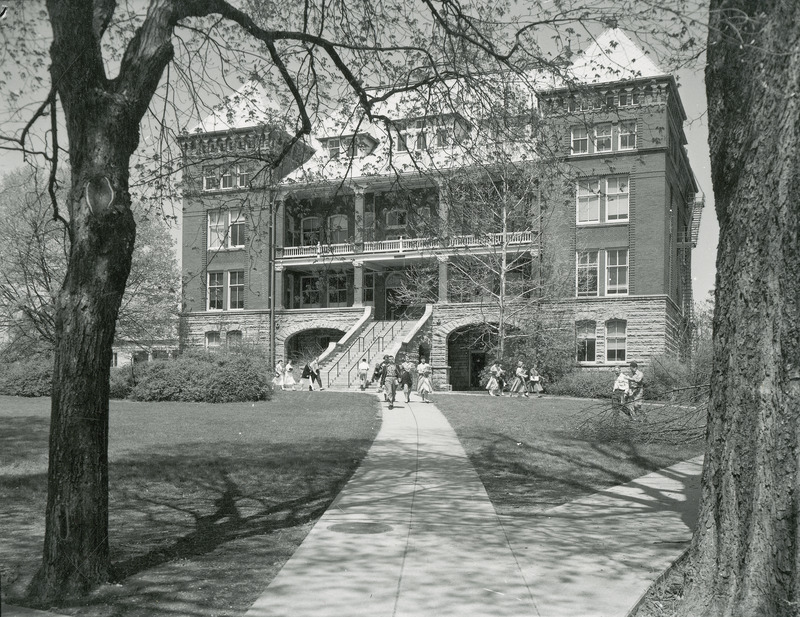 The front of Catt Hall. Groups of individuals are walking on the sidewalk. A small portion of MacKay Hall can be seen in the background.