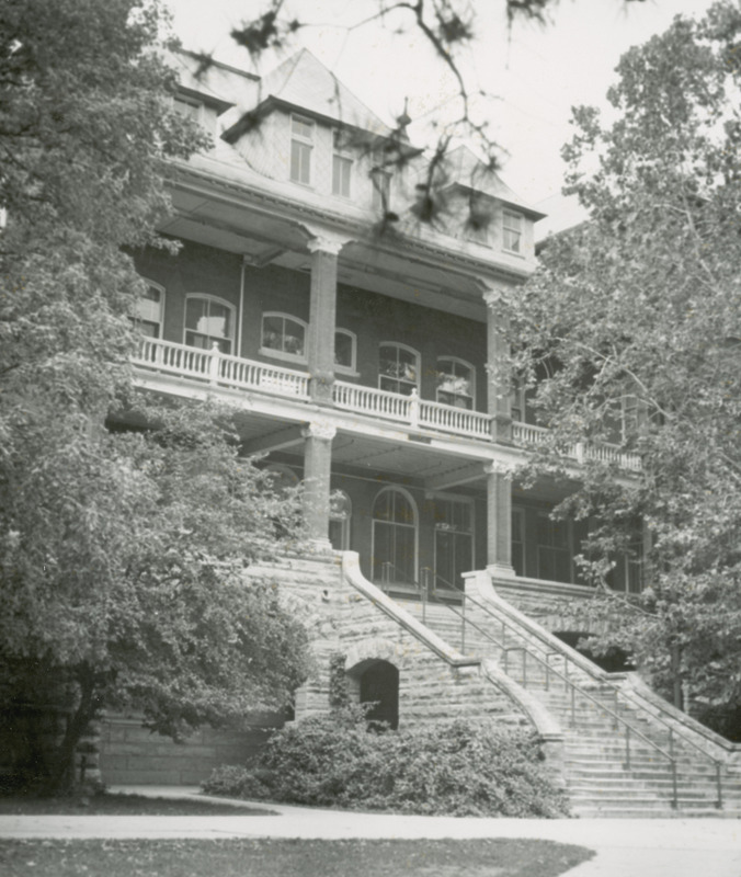 This focus of this image is the front of Catt Hall. The front stairs and balcony can be seen, however the surrounding tree obscure part of the view.