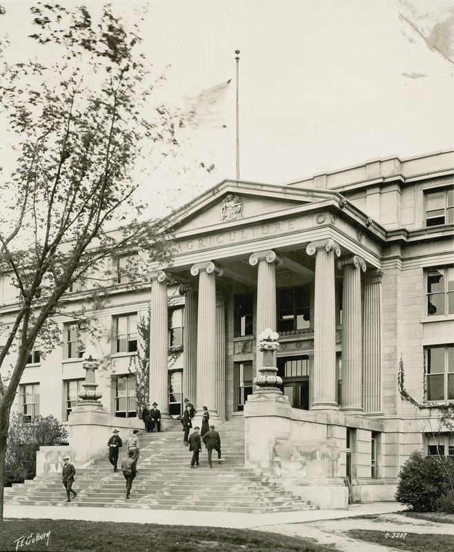 Eleven men and women students use the steps of Agriculture Hall (Curtiss Hall) while the flag above the pediment flies at half-mast.