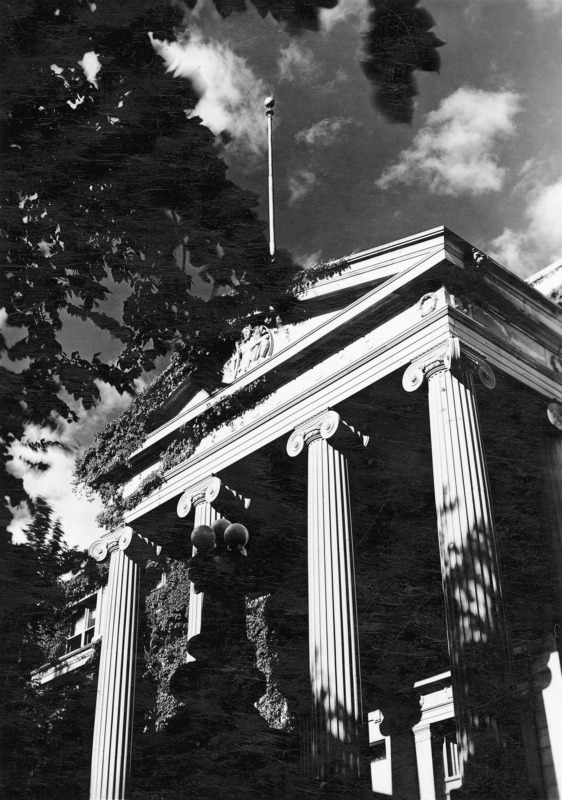 The four columns of the Curtiss Hall portico are highlighted in the sun under the crowning pediment and flagpole, with trees and ivy on the left.