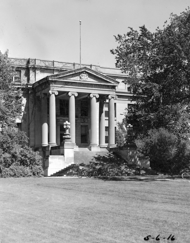 Bicycles are parked in the shade of a large tree in front of the entrance to Curtiss Hall.