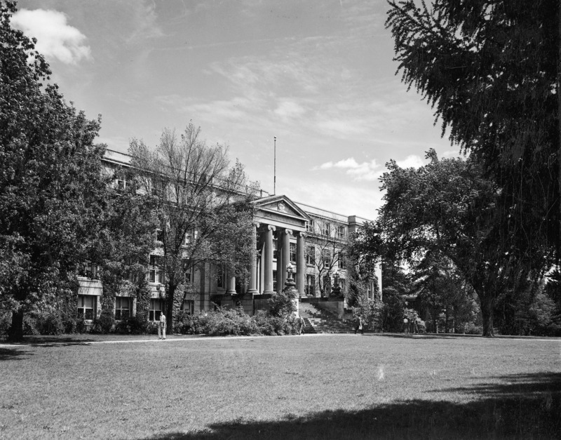 Curtiss Hall is viewed from the northwest, showing the west elevation, as students walk by the building and budding trees.