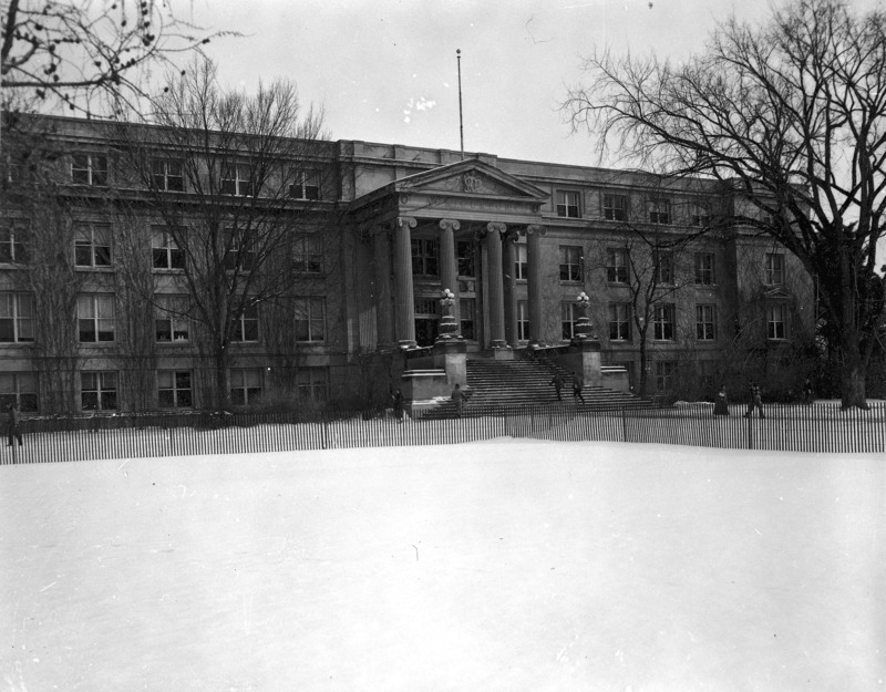 The front (west) facade of Curtiss Hall is viewed from snowy central campus behind a snow fence, with students rushing by.