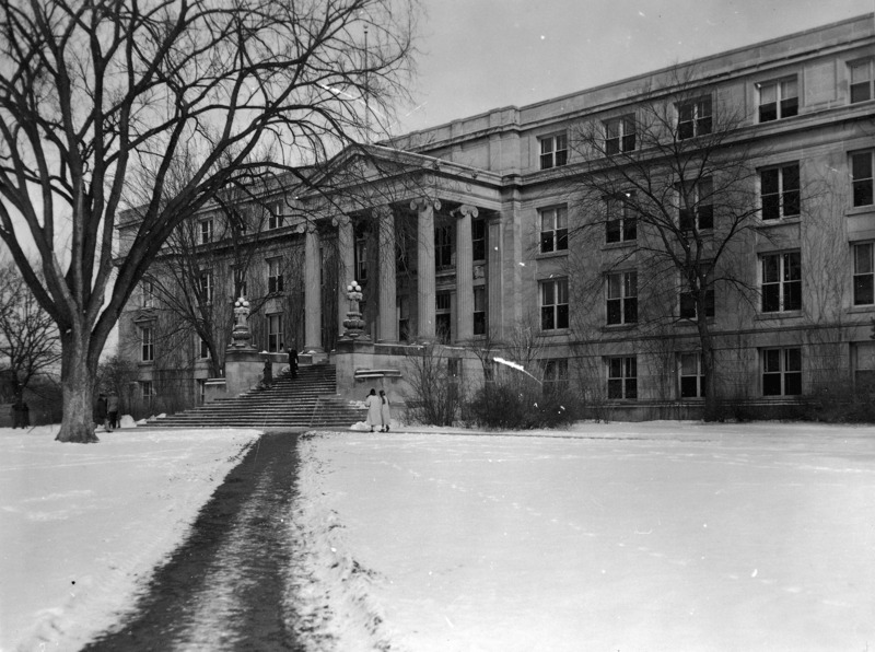 Curtiss Hall is viewed from the sidewalk leading to it from the southwest, as people walk by in the snow.