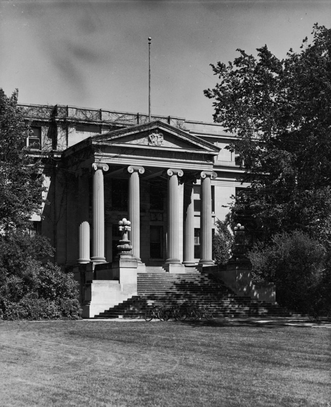 Bicycles are parked in the shade of a large tree in front of the entrance to Curtiss Hall, headquarters of the Division of Agriculture.