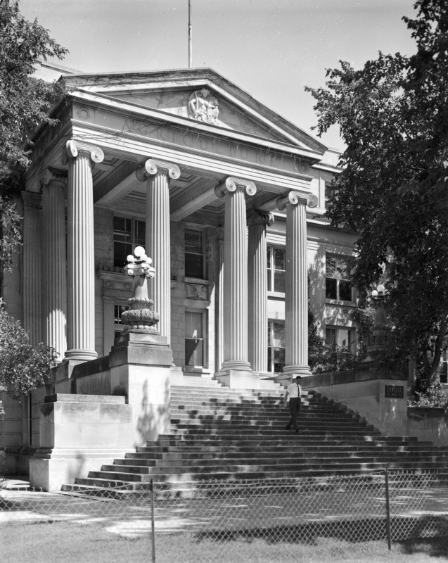 A man walks down the steps of Curtiss Hall, which has a chain link fence in front of it.