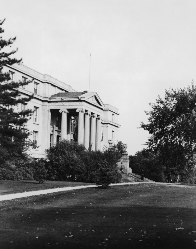 The front (west) facade of Agriculture Hall (Curtiss Hall) is viewed from the northwest, with leaves on the ground and people walking by. Two new trees have been planted on either side of the sidewalk.