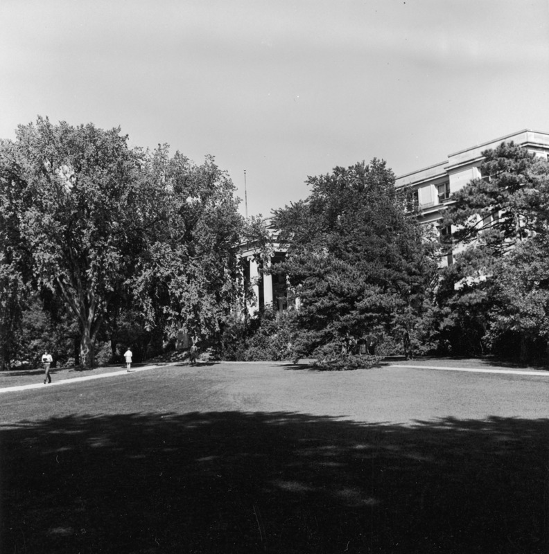 Curtiss Hall is viewed through large trees on the southwest as students in 1960s clothes and hairstyles pass by on the sidewalk to the Campanile.