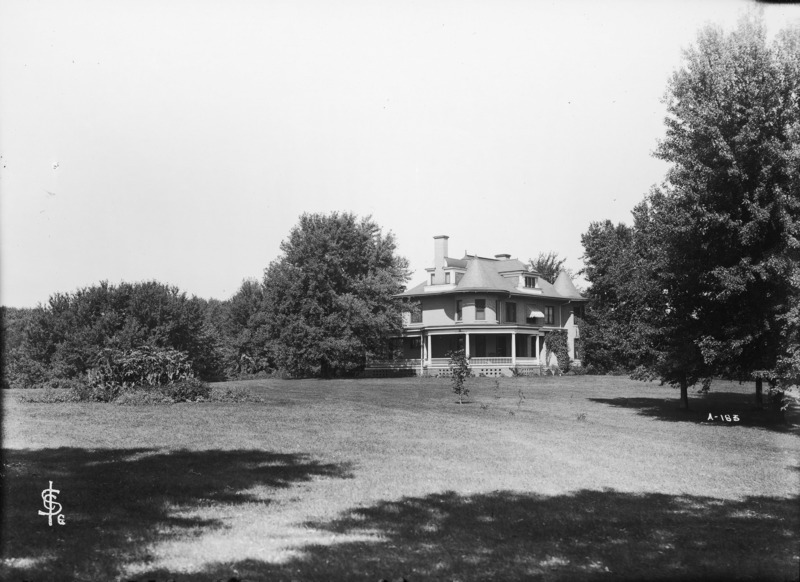 The southeast corner of the Knoll appears in the distance surrounded by trees and other shrubbery. A large expanse of lawn occupies the foreground.