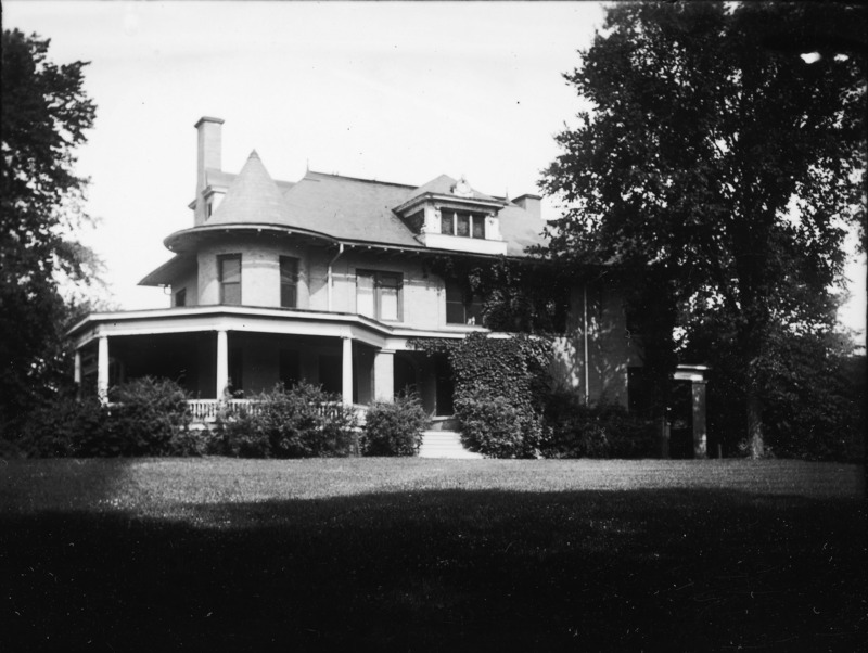 The front of the Knoll is partially hidden by trees. The front entryway, wrap around porch and upper floors are visible.