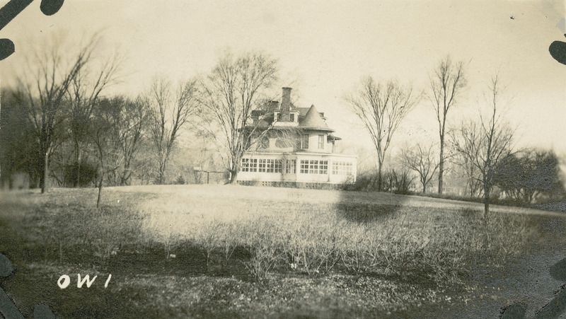 The south side of the Knoll is in the distance with the lawn in the foreground. A glassed-in porch stretches along the entire south side of the ground floor.