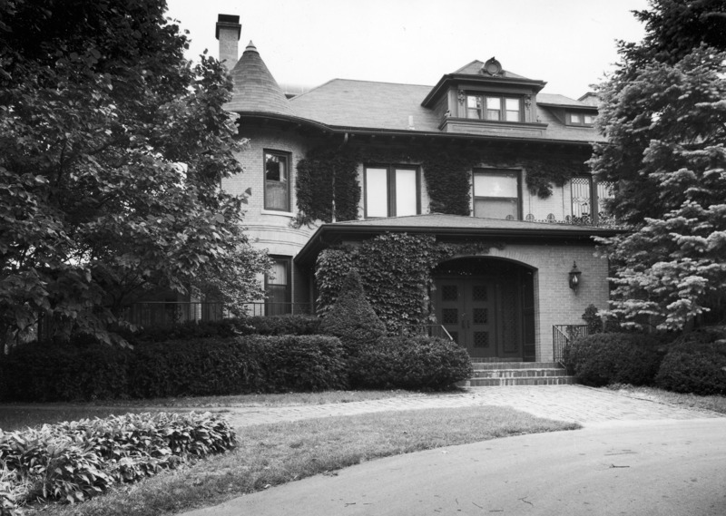 A brick sidewalk and paved driveway go past the east side of the Knoll. The entryway is partially covered with climbing ivy and much of the building is hidden by trees and bushes.