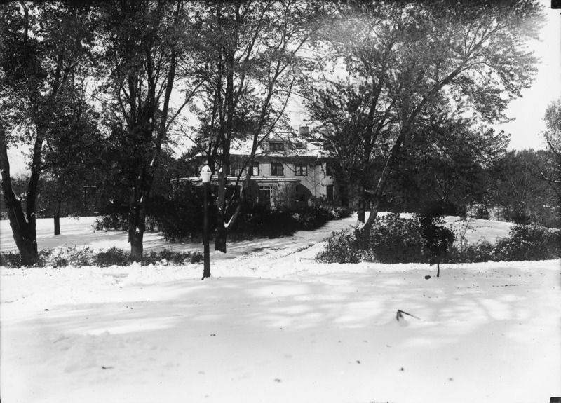 This winter scene shows the north side of the Knoll surrounded by trees. There is a light post in the center of the frame. The ground and building are covered in snow.