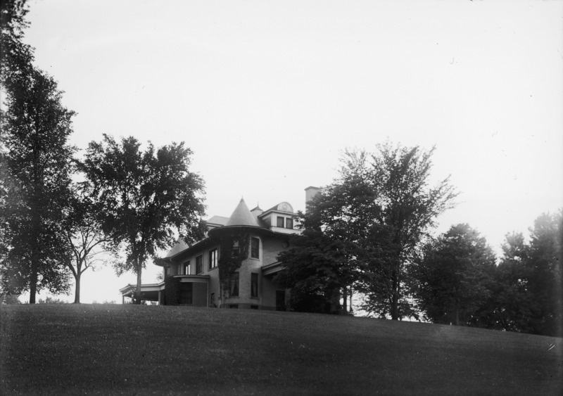 A ground view of the northeast corner of the Knoll. Trees surround the building and the tower is partially covered in climbing ivy. The lawn occupies the foreground of the image.