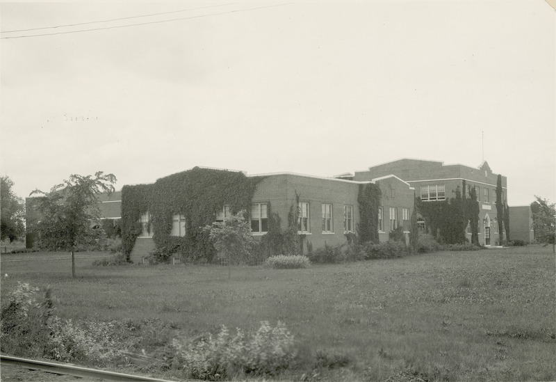 Viewed from the southeast, the east wing and the main building of the Quadrangle (later known as Lagomarcino Hall) are covered in ivy. The Ames and College Railroad tracks are partially visible in the lower left of the photograph, 1920.