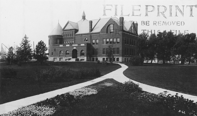 Two flower-lined sidewalks lead up to Morrill Road and the main entrance of Morrill Hall. A row of trees stand to the north side of the building and the construction of Central Building (Beardshear Hall) is beyond.