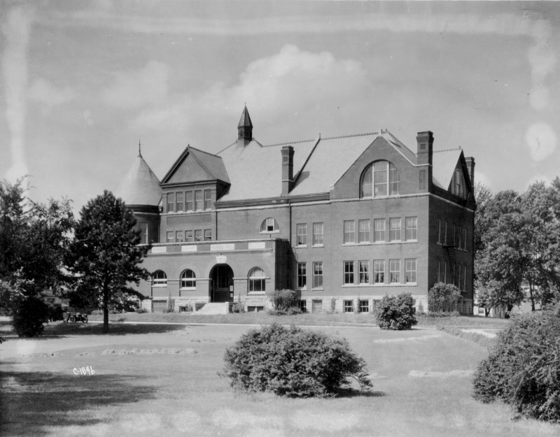 The tower of Morrill Hall is partially obscured by trees. A period automobile is parked under the trees.