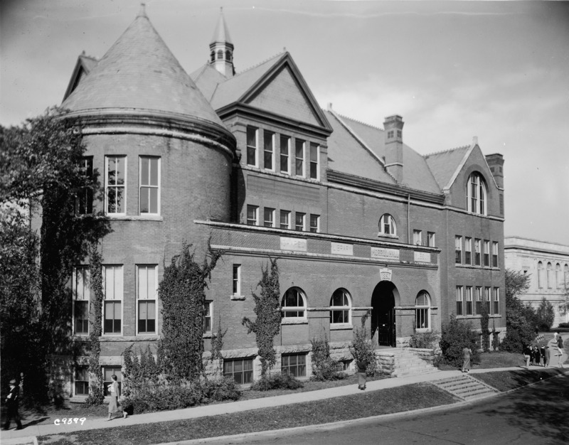 Individuals in period attire are walking by Morrill Hall. Ivy can be seen growing on the wall of Morrill Hall in this southeast view. A portion of the college/university Library (Parks Library) is visible to the north.