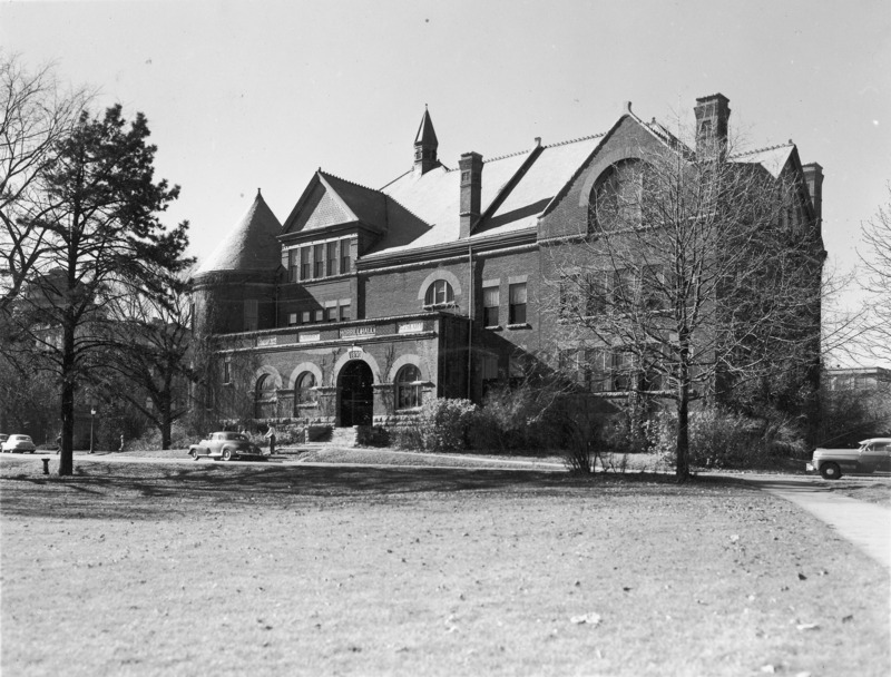 Two individuals are standing near a 1940s automobile parked in front of Morrill Hall.