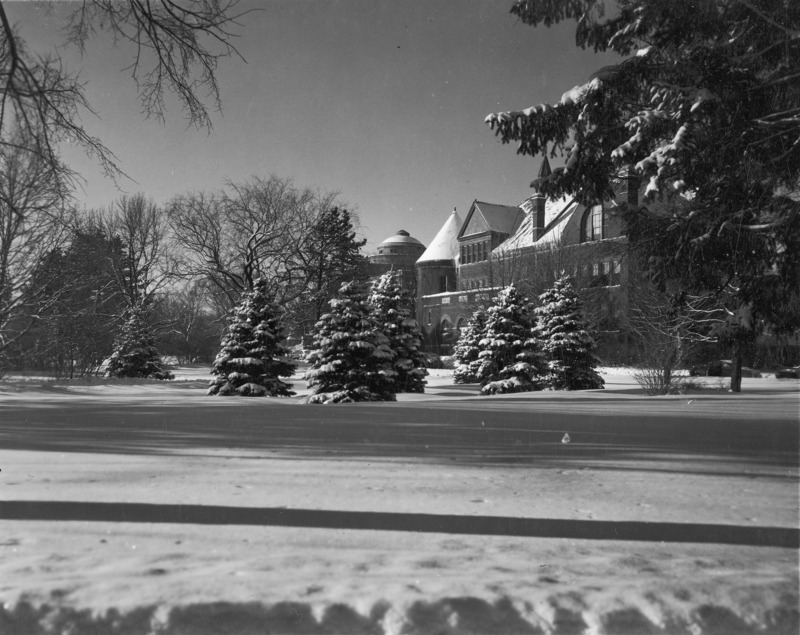 Snow-covered trees partially obstruct the view of the entrance to Morrill Hall. The top of the Morrill tower and the dome of Central Building (Beardshear Hall) are visible in the center of the photo.