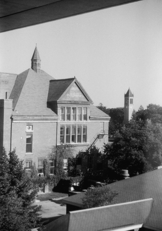 The Campanile can be seen in the distance in this aerial view of the west side of Morrill Hall. Ivy is growing on the outside of the building. The roof of the Hub is in the foreground.