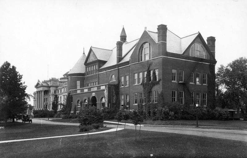 Period automobiles are parked in front of Morrill Hall and ivy is growing along the walls. The front of Central Building (Beardshear Hall) can be seen in the background.