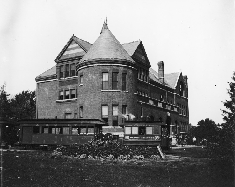 The Ames and College Railway (the Dinkey) car is stopped near Morrill Hall. A floral garden is planted along the tracks.