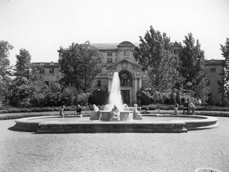 This 1941 photograph shows a close view of the Four Seasons Fountain in the front (north) of the Memorial Union. The Four Seasons Fountain, which includes four Native American female figures, each representing one of the four seasons, is by Christian Petersen. Five individuals sit or stand around the edge of the fountain. The Union building, partially hidden by trees and plantings and the fountain's water spout, is in the background.