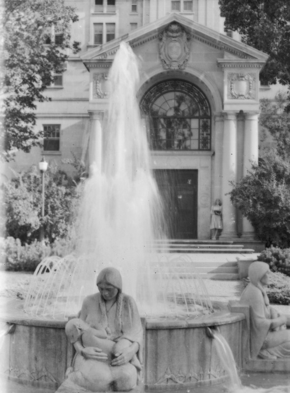 This 1941 image is a close-up of two of the figures, Winter and Fall, in the Four Seasons Fountain which is located in front (north) of the entrance to the Memorial Union's Gold Star Hall. The Four Seasons Fountain, which includes four Native American female figures, each representing one of the four seasons, is by Christian Petersen. The Gold Star Hall entrance is in the background, and a solitary woman leans against one of the columns, reading.