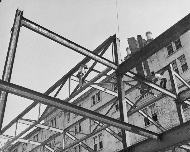 This 1951 photograph shows the steel framework for the northwest addition. Two workmen are on the framework and the Memorial Union building is in the background.