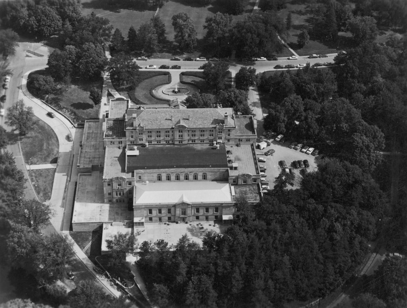 This 1954 aerial view of the Memorial Union from the back (south) clearly shows the multiple stories and roof levels, the terrace to the left (west) side, the parking lot on the right (east) side, and the fountain in the front (north). The formal courtyard design around the fountain is evident. Cars are on the streets and lot near the building.