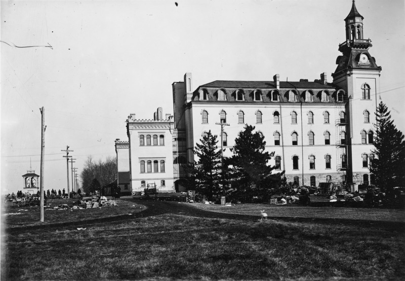 The south side of the south wing of Old Main after the first fire in December 1900. A large amount of room furnishings are strewn around the grounds. This view shows clearly that the south wing was the least affected portion of the building in the first fire.