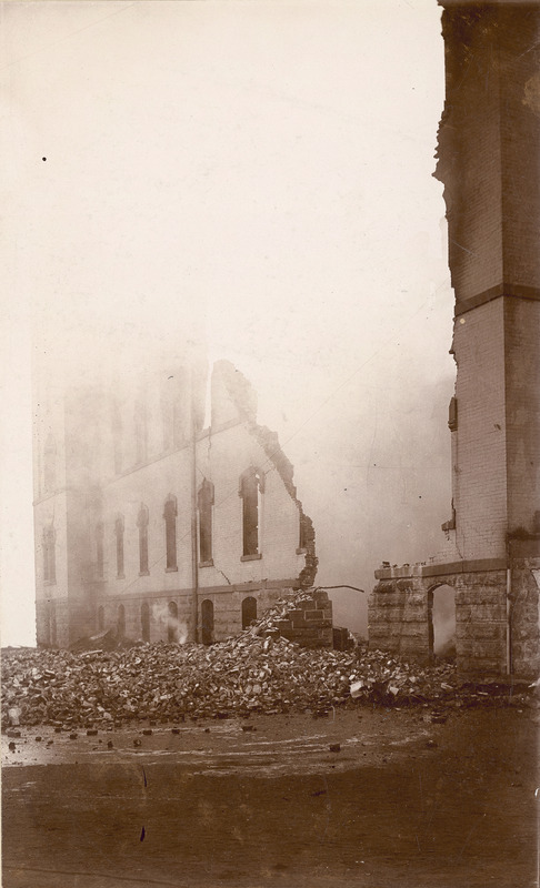 A collapsed wall after the first building fire at Old Main in December 1900. A large amount of rubble is at the base of the large open space in the wall. Smoke is still present inside the burned out building wing.