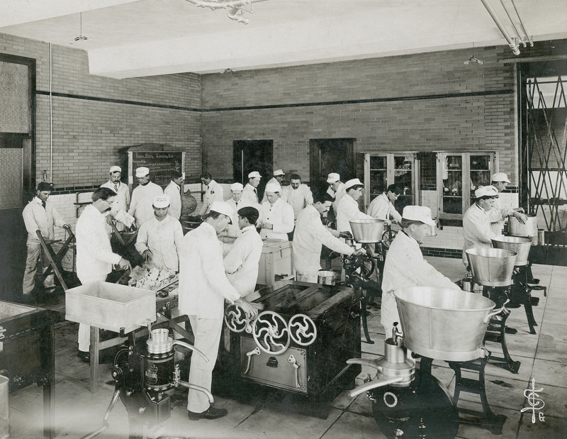 Several people wearing white coats and hats are working on various pieces of equipment located in the old Dairy Industry building (East Hall).