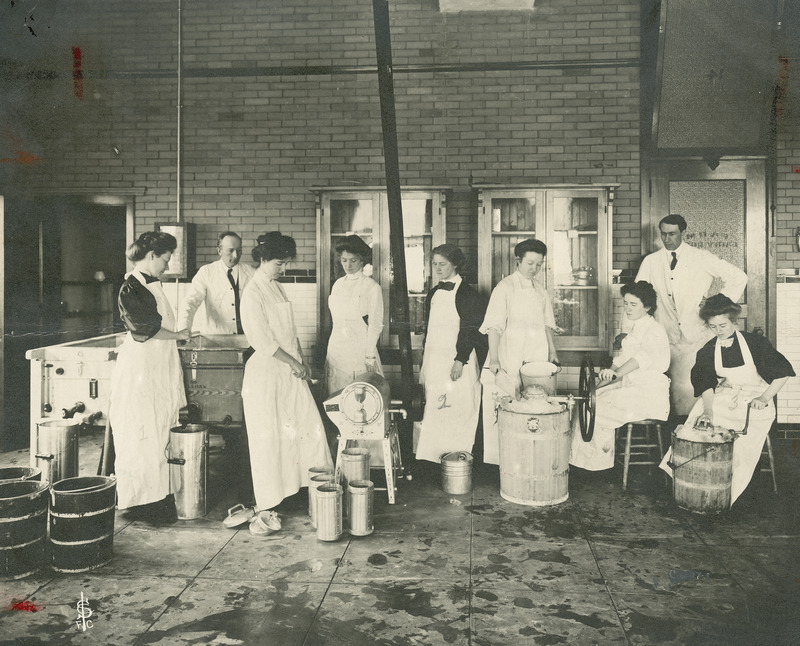 This photograph shows Martin Mortensen (2nd from left, standing behind the vat), professor of dairy for over 40 years at the Iowa State College (University) teaching a class of eight women and one male student how to make ice cream and ices in the Agricultural Annex. Two of the women students are shown turning the handles of ice cream makers that are packed with ice.