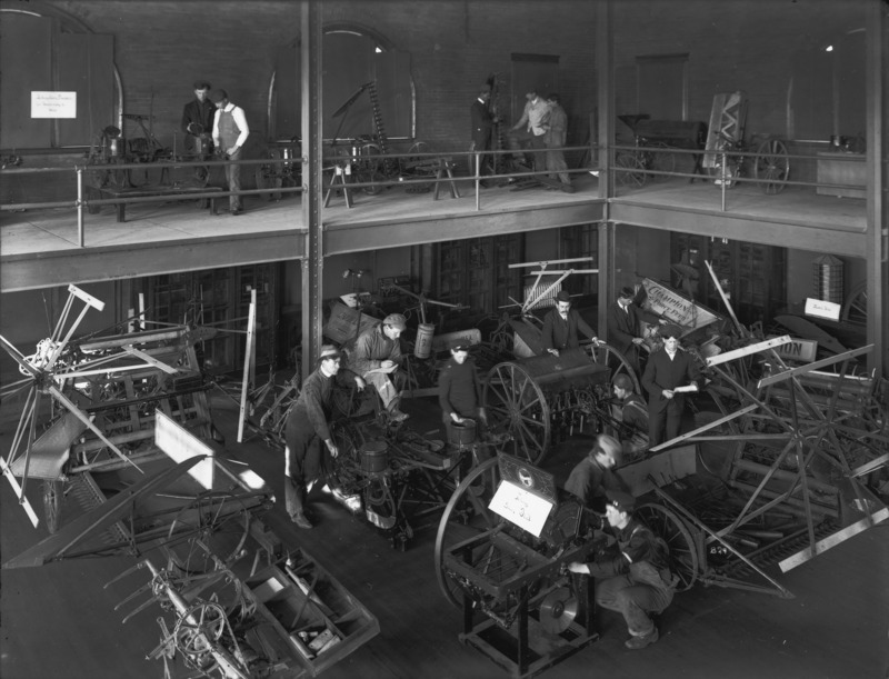 A farm machinery exhibit indoors. The machinery is exhibited inside an open industrial space with two floors. November 1904.