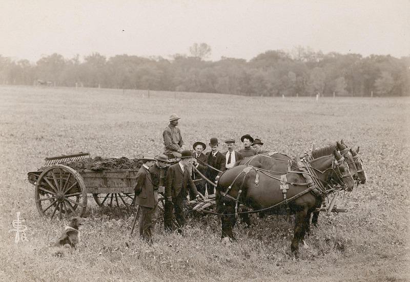 Seven men and a dog are pictured. Testing of a three-horse manure spreader, October 15, 1906.