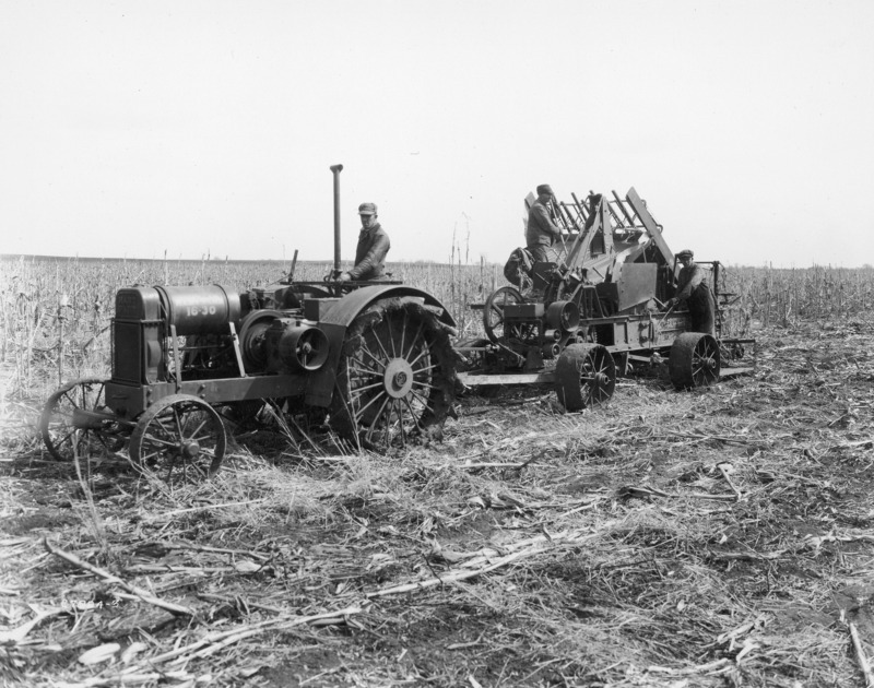 A Hart-Parr 16-30 steel-wheeled tractor pulling a corn stalk harvesting machine. The corn field has already been harvested for corn. One man is driving the tractor and two other men are working on the stalk harvester. The photograph was taken April 12, 1928.