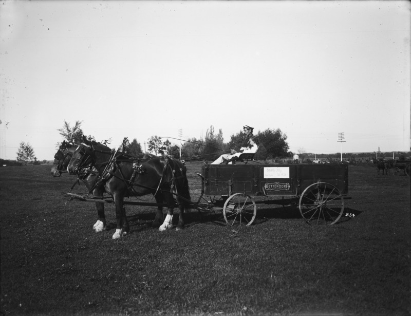 A two-horse team hitched to a Bettendorf utility wagon. The driver and a child are posing in the driver's seat. The photograph was taken in the fall of 1904, probably on Excursion Day.