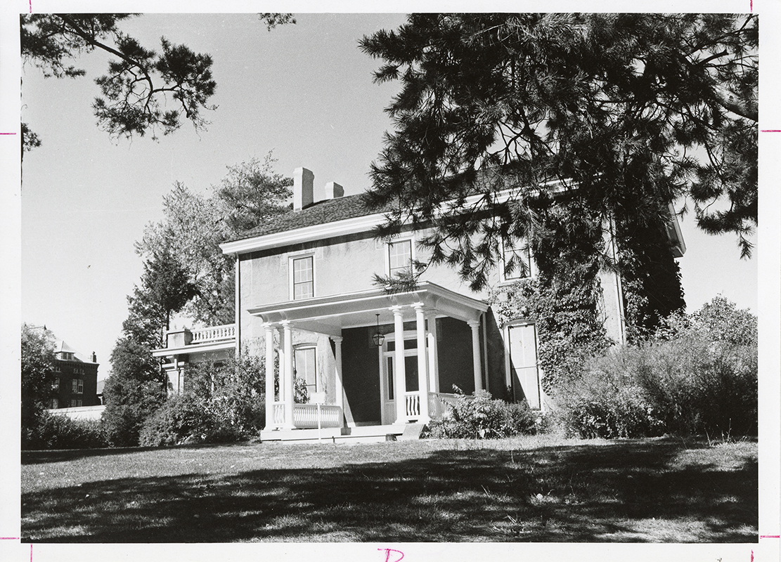 Photograph looking north-west at the front porch and south side of the Farm House. Part of Catt Hall can be seen in the background to the left (north-west) of the Farm House. Annotation: "Farm House."