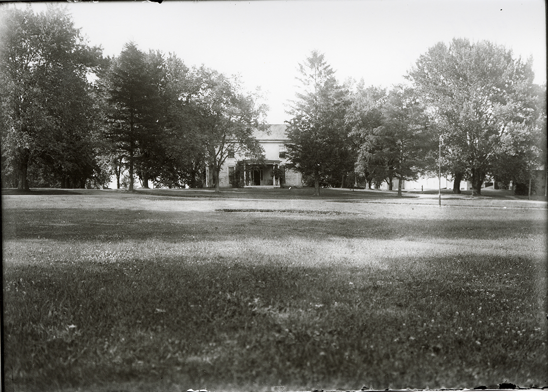 Photograph of the front of the Farm House showing the lawn in front of the house. Annotation: “Farm House. Horse & Cattle barns in background on right. n.d.”