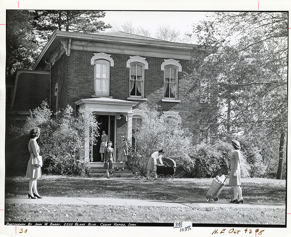 Photograph of women outside Sloss House while it was being used as a home management house. One woman leans over a baby carriage, while others stand on the steps and sidewalk. 