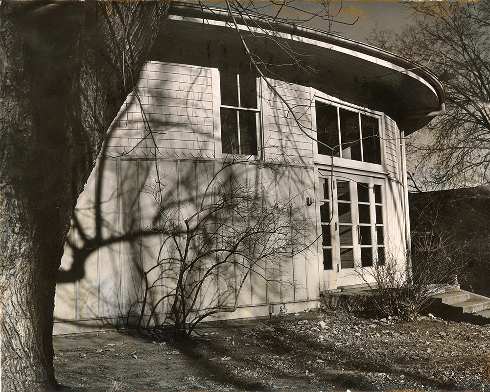Photograph of the south doors of the Shattuck Theatre. There are trees and bushes without leaves in the foreground. 